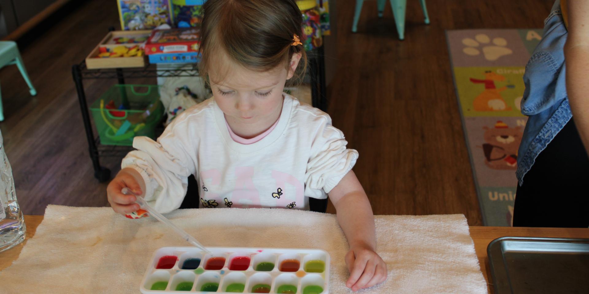 Girl with ice cube tray and color liquids